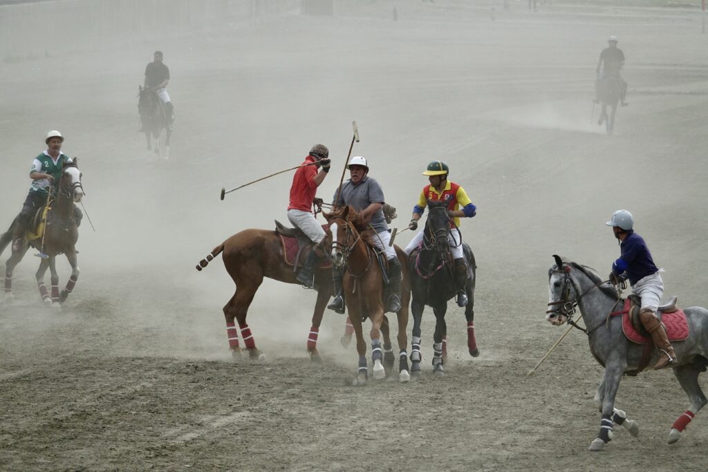 Three polo players are riding horses in the sand.