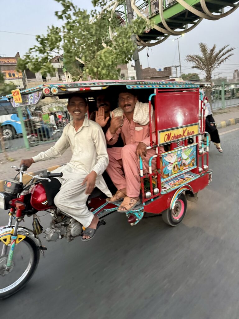 Three men riding a red rickshaw on the street.
