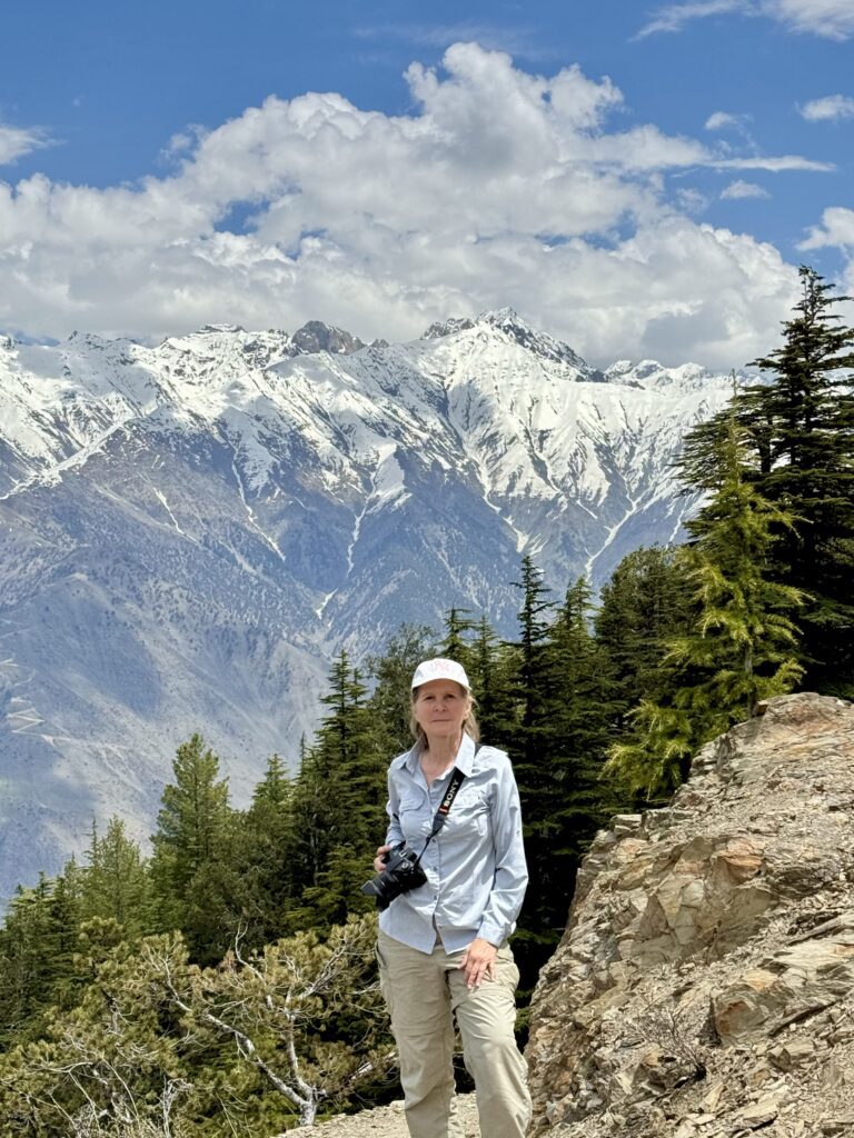 A woman standing on top of a mountain with snow covered mountains in the background.