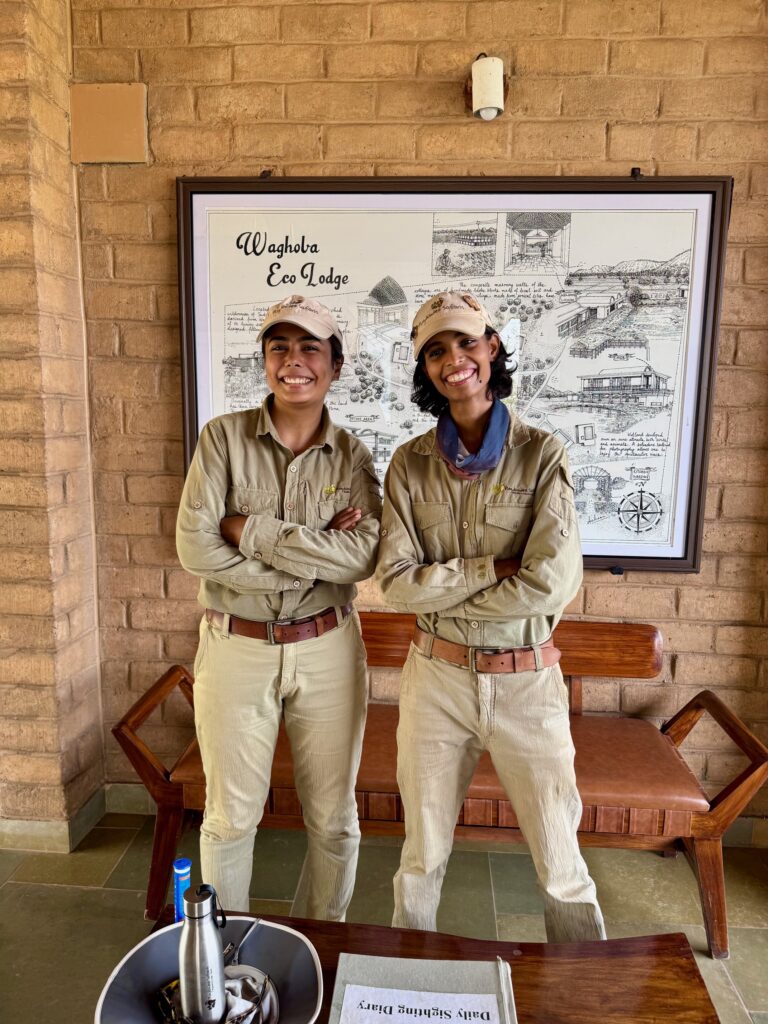 Two people in matching safari outfits standing indoors with arms crossed.